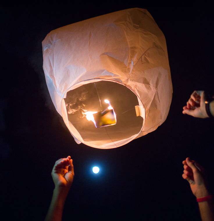 several people releasing lanterns into the sky at night with one candle lit in the air