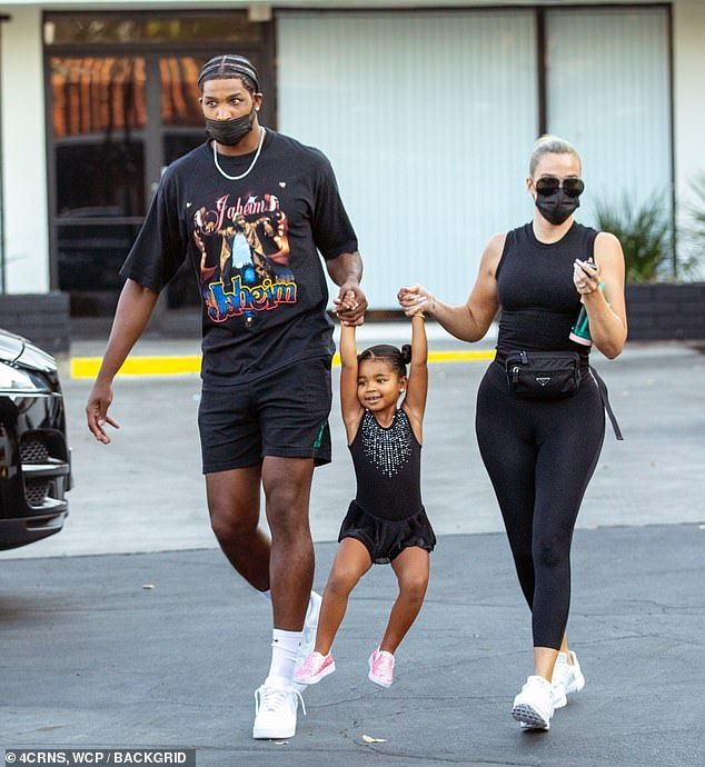 a man, woman and child walking in front of a black car wearing face masks