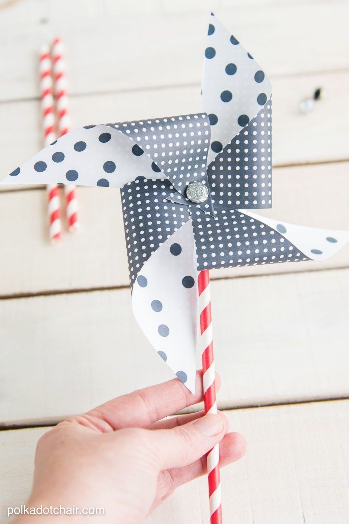 a hand holding a pinwheel on top of a white wooden table with red and blue striped straws