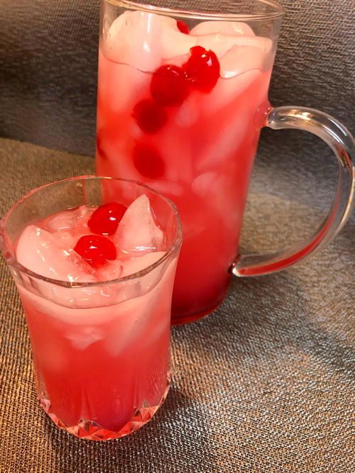 two glasses filled with ice and cherries next to each other on top of a table