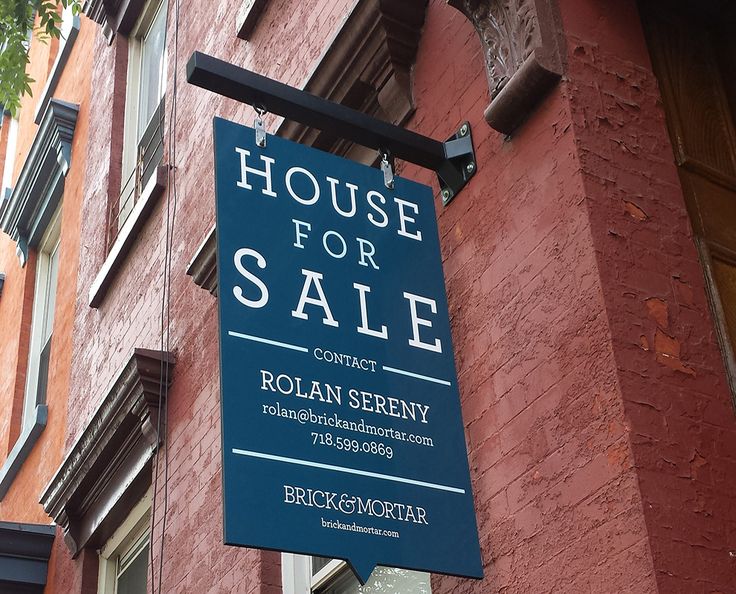 a house for sale sign hanging from the side of a building