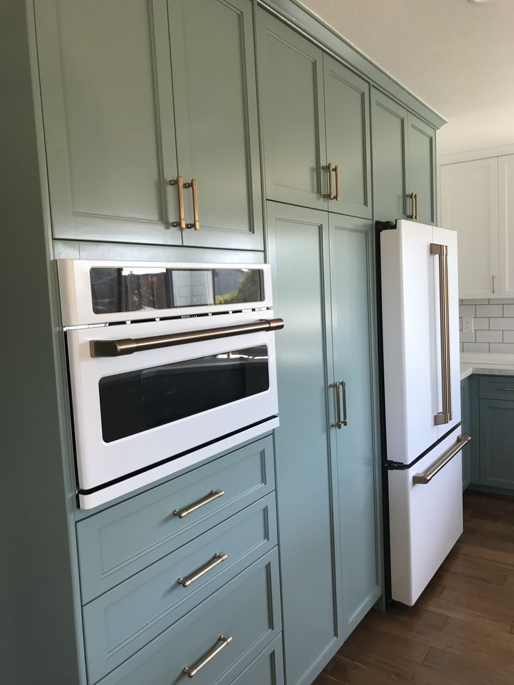 a kitchen with green cabinets, white appliances and wood flooring is pictured in this image