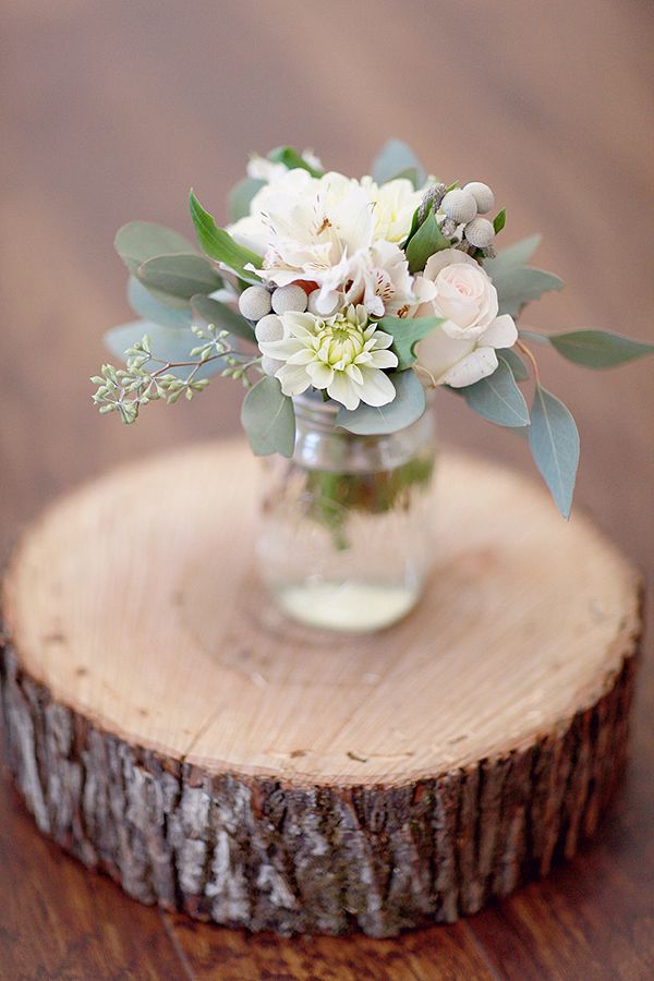 a glass vase with flowers and greenery is sitting on a tree stump