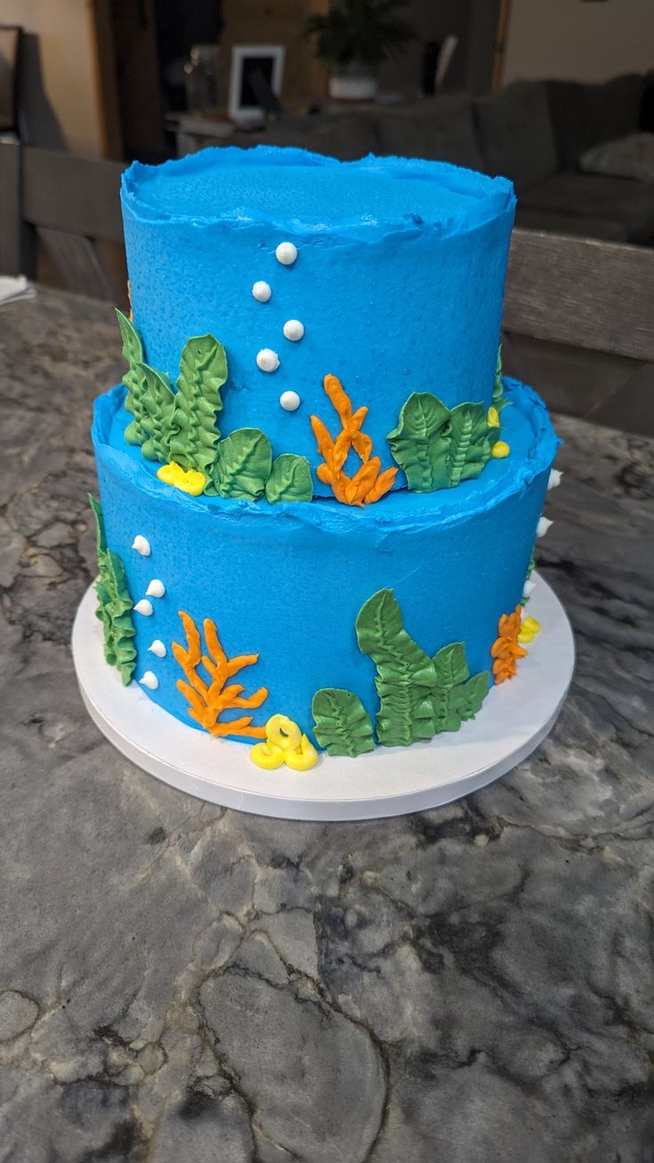 two tiered cake decorated with blue frosting and seaweed on a white plate