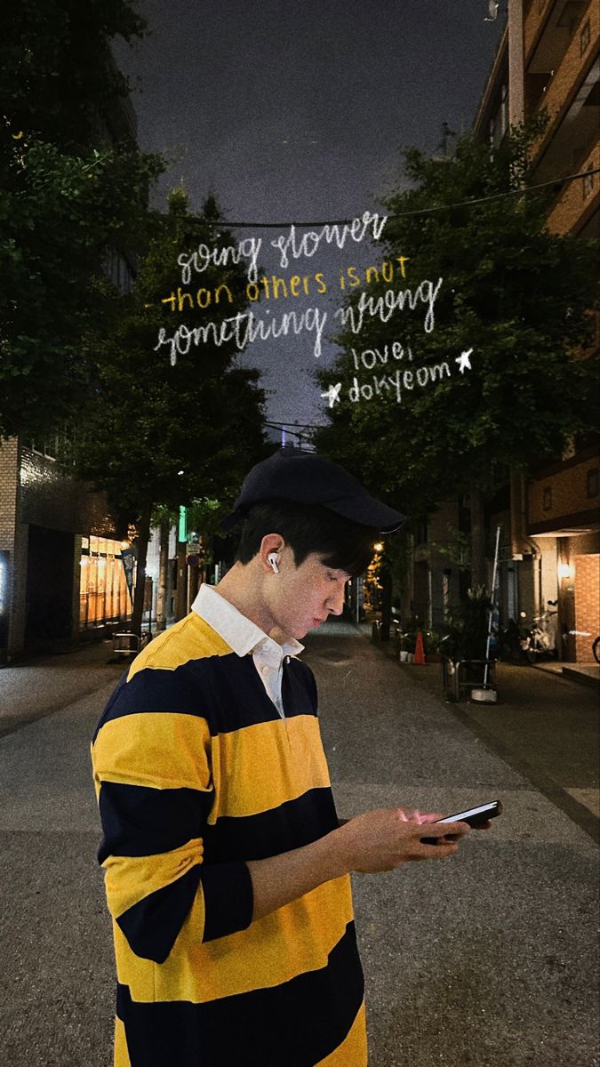 a man in a yellow and black striped shirt looking at his cell phone while standing on the street