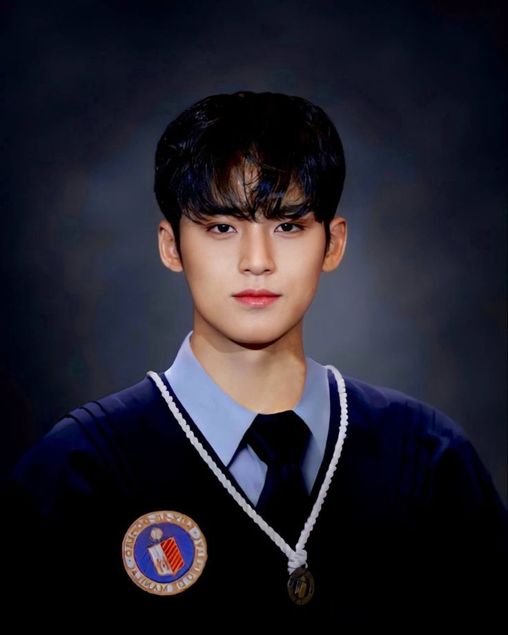 a young man wearing a blue shirt and black tie with badges on his collar, standing in front of a dark background