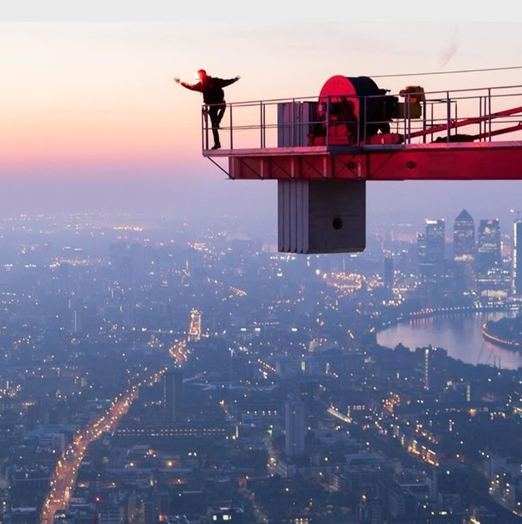 a man standing on top of a tall tower next to a cityscape at dusk