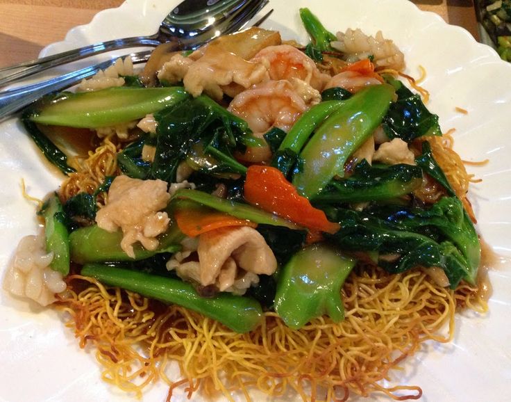 a white plate topped with noodles and vegetables next to a silver fork on top of a wooden table