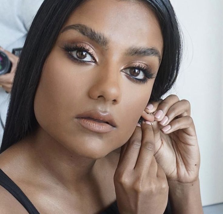 a close up of a person with a camera in the background and one hand on her face