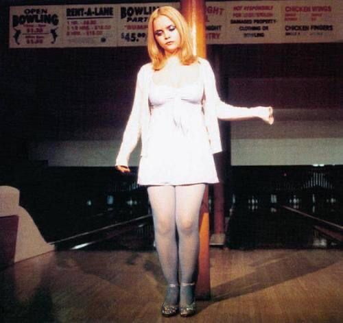 a woman standing in front of a bowling alley with her arms out and legs crossed