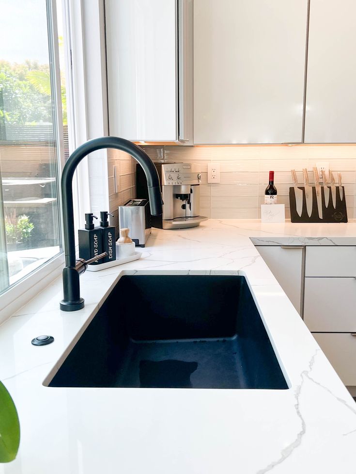 a white kitchen with marble counter tops and black faucet in the sink area