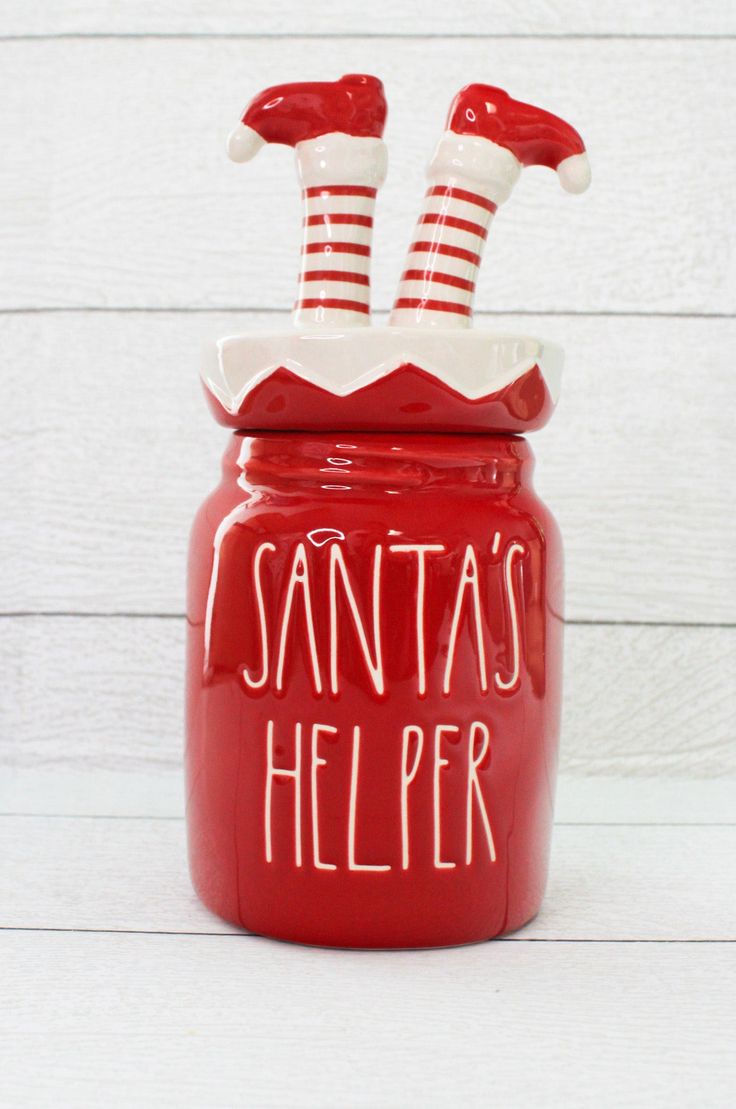 a red santa's helper jar with stockings on top that says santa's help