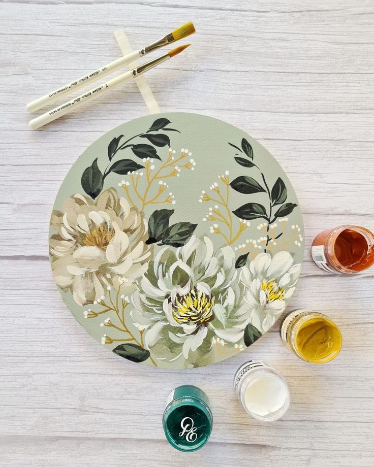 the paint and brushes are sitting on the table next to the painted plate with flowers