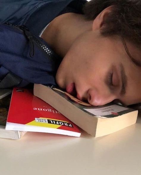 a young man sleeping on top of books with his eyes closed and head resting on the book