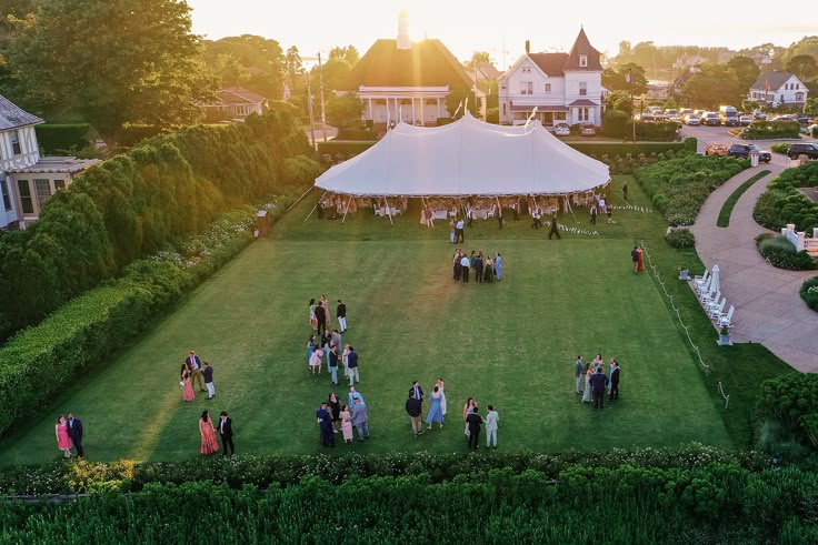 a group of people standing on top of a lush green field next to a white tent