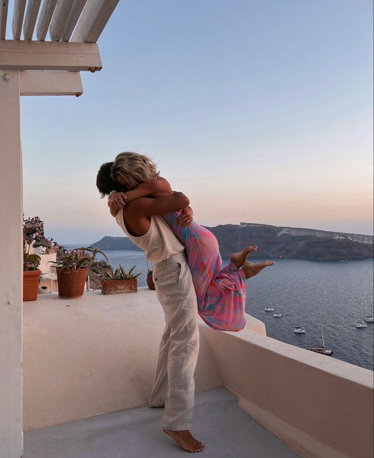 two people embracing each other on a balcony overlooking the ocean