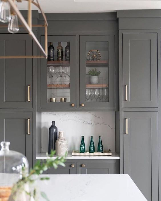 a kitchen with gray cabinets and marble counter tops, green vases on the bar