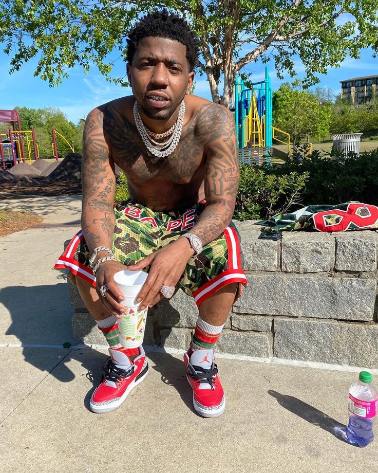 a man with tattoos sitting on the ground next to a skateboard and water bottle