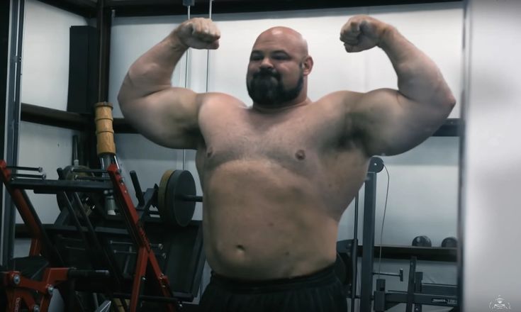 a man with no shirt on is flexing his muscles in the gym while holding a barbell