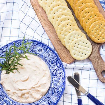 two crackers and a bowl of dip on a blue plate with utensils