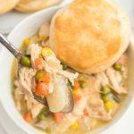 a white bowl filled with chicken pot pie soup and a roll on the side next to it