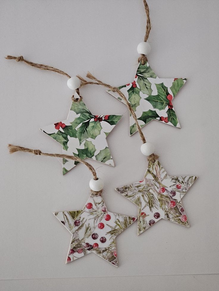 three christmas decorations hanging from twine with holly leaves and berries on them, one star shaped ornament