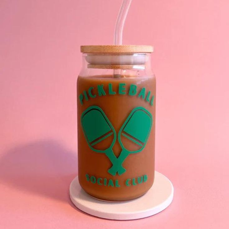 a jar with a straw in it sitting on top of a pink surface next to a cup