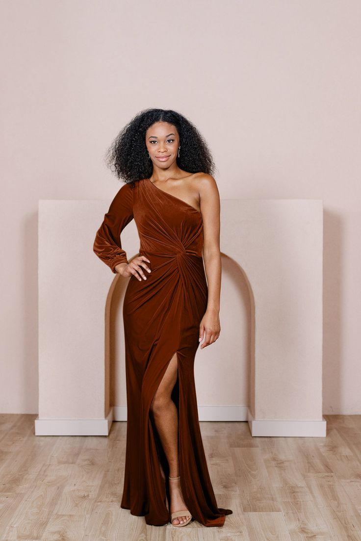 a woman standing in front of a wall wearing a brown dress