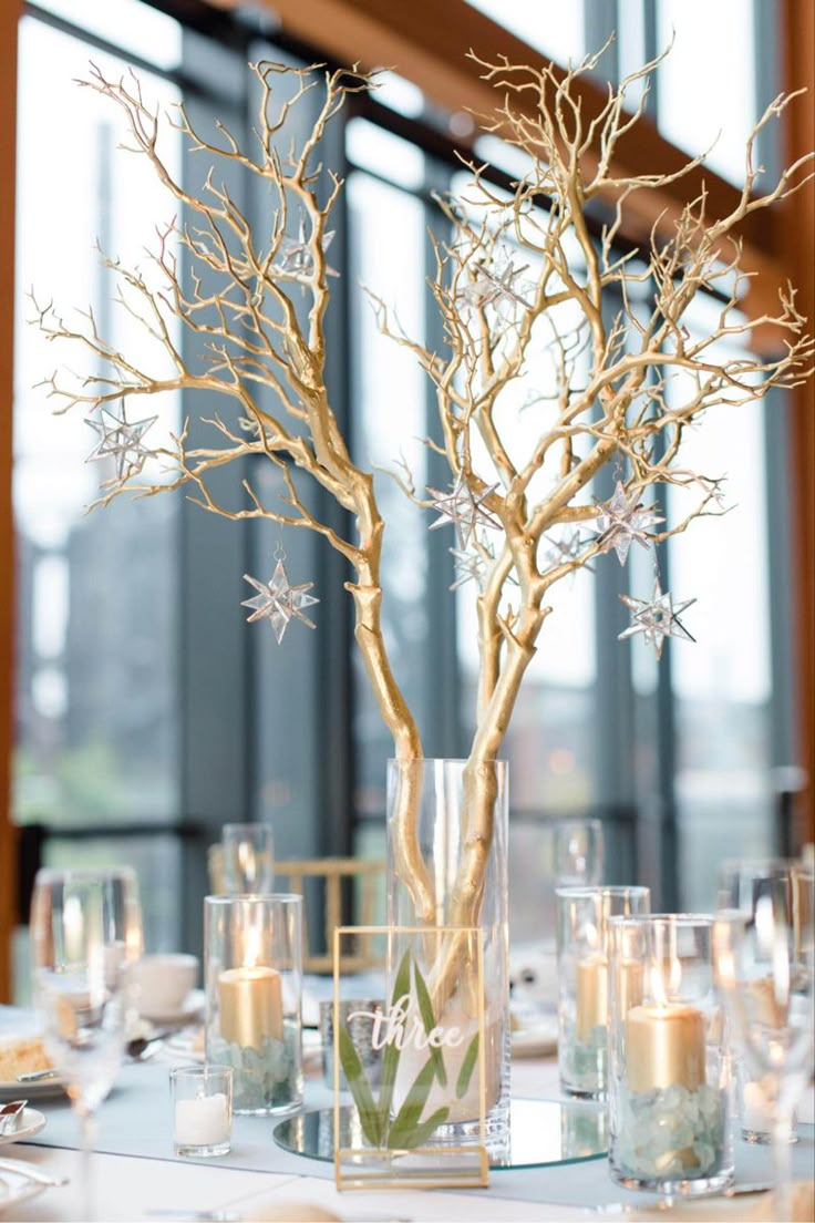 a centerpiece with branches and candles is displayed on a table in front of large windows