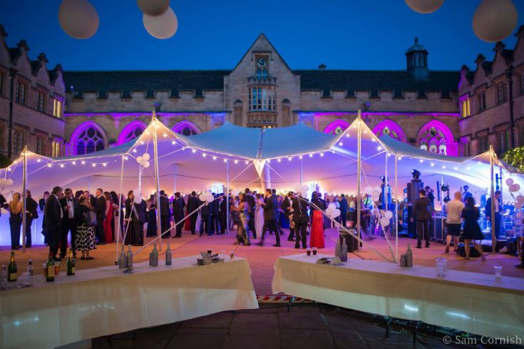 a group of people standing under tents in the middle of a courtyard with lights on them