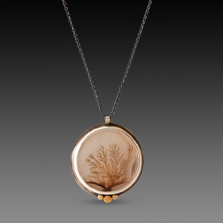 A very special dendritic agate evokes a mysterious and lovely scene in nature. The stone is wrapped in sterling silver and accented with a hammered 22k gold trio. Each of these incredible stones is one of a kind, and completely natural. Pendant measures approximately 7/8 inch in diameter, and is suspended from an oxidized sterling silver chain. Matte finish. This piece is in stock and ready to ship.