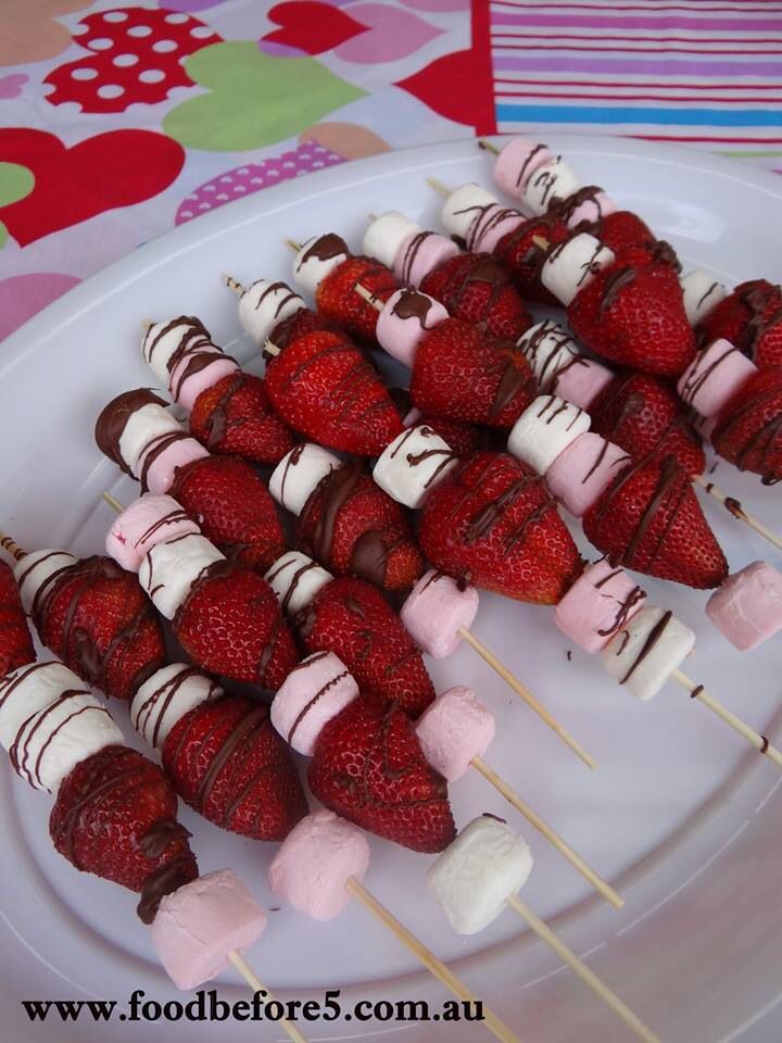 strawberries and marshmallows are on skewers on a white plate