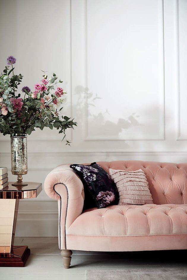 a pink couch sitting next to a vase with flowers