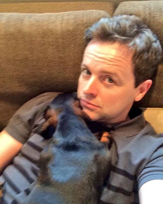 a man laying on top of a couch next to a black and brown dog in his lap