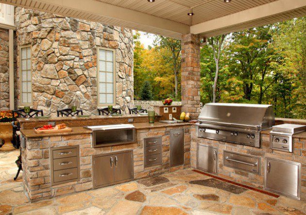 an outdoor kitchen with stainless steel appliances and grilling area in front of stone wall