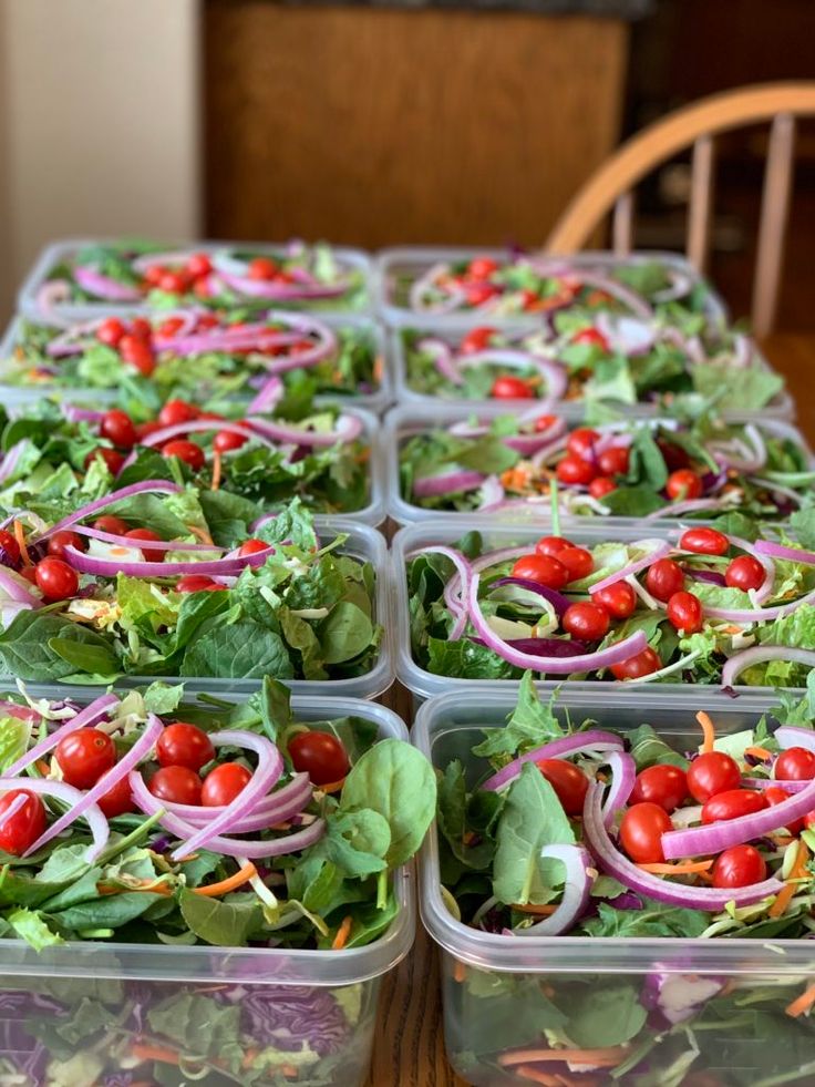 several plastic containers filled with salads on top of a wooden table