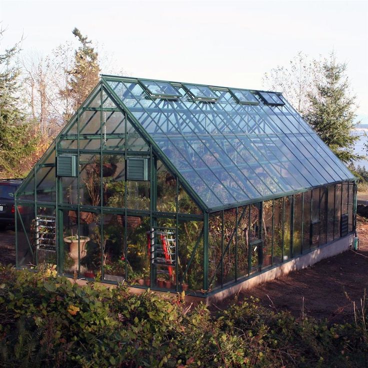 a large green house sitting in the middle of a field next to some bushes and trees