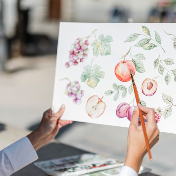 two people holding up an art piece with fruit on it and one person drawing something