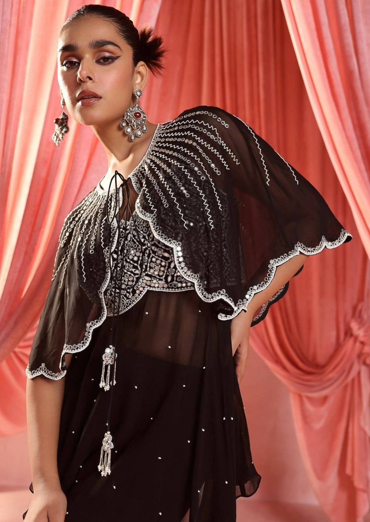 Embellished cape paired with an embellished peplum and gharara. Evening Cape Sets Made Of Georgette, Eid Evening Sets With Cape Sleeves, Evening Sets For Eid With Cape Sleeves, Evening Sets With Cape Sleeves For Eid, Eid Party Cape Sets, Festive Georgette Cape Sets, Festive Evening Set With Cape Sleeves, Glamorous Hand Embellished Sets For Eid, Bollywood Style Cape Sets For Party