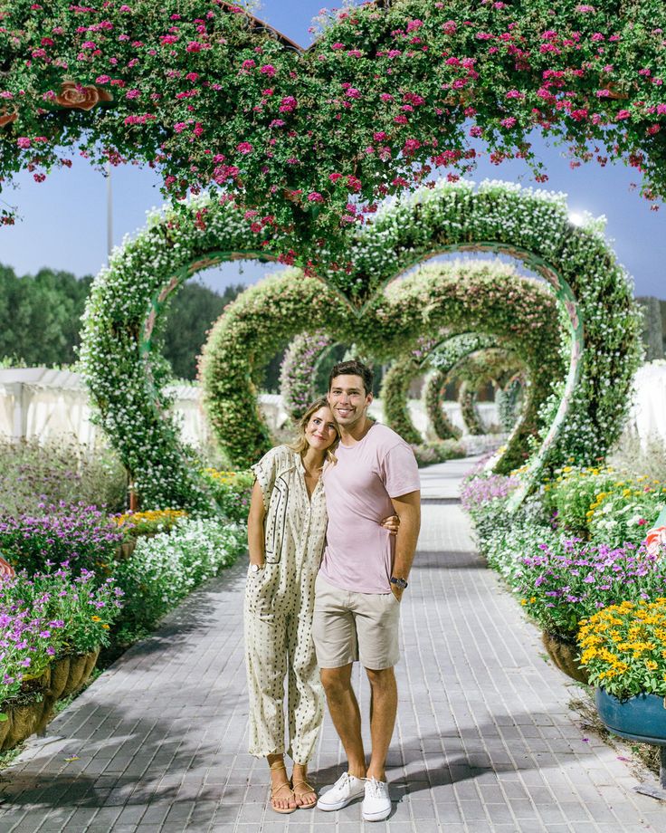 a man and woman standing in front of a heart - shaped archway covered with flowers