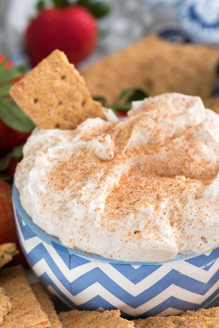 a bowl filled with whipped cream surrounded by crackers and strawberries