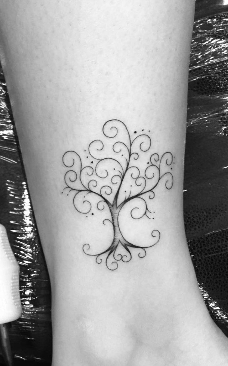 a small tree tattoo on the ankle with swirls and curls around it's branches