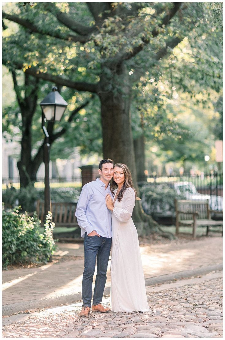 an engaged couple standing in front of a tree