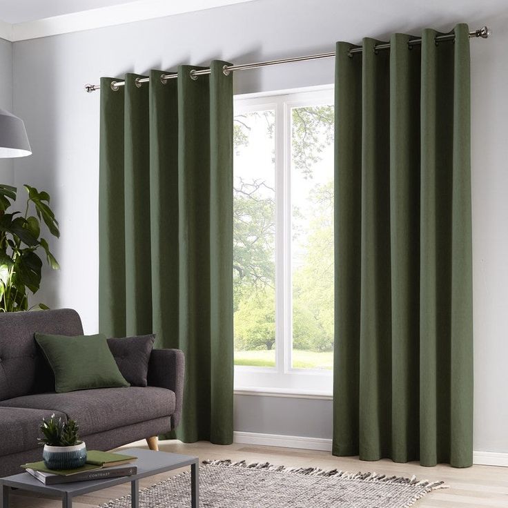 a living room with green curtains and a gray couch in front of a large window