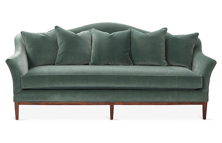 a green velvet couch with six pillows on it's arms and back, against a white background