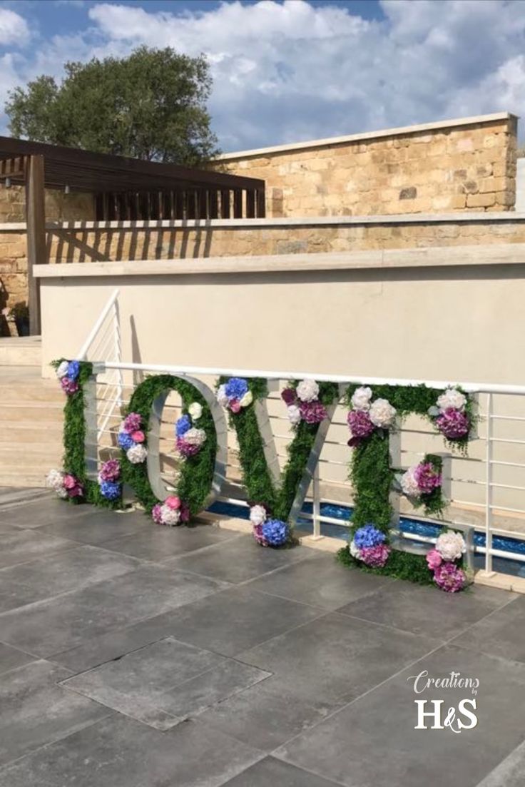 the word love is made out of flowers and greenery in front of a building