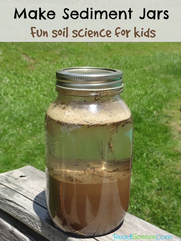 a jar filled with brown liquid sitting on top of a wooden table next to grass