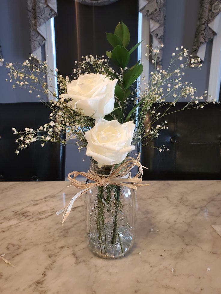 three white roses in a glass vase with baby's breath tied around the stems