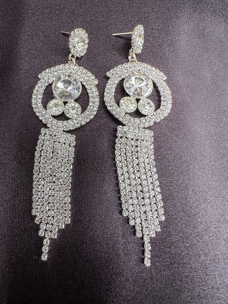 Embrace elegance with our sparkling rhinestone earrings, the perfect accessory to elevate any outfit for a night out. These dazzling dangle earrings effortlessly blend fashion and sophistication, adding a touch of glamour to your look. Make a statement with these stunning earrings that will enhance your style and make you stand out in any crowd. Elevate your ensemble and shine bright with these exquisite rhinestone earrings. Ready to be shipped Diamond White Crystal Earrings For Party, Glamorous Crystal Dangle Bridal Earrings, Glamorous Crystal Drop Earrings, Glamorous Sparkling Dangle Diamond Earrings, Glamorous Crystal Chandelier Earrings With Rhinestones, Silver Rhinestone Earrings For Glamorous Events, Sparkling Crystal Clip-on Earrings Glamorous, Dazzling Dangle Crystal Earrings, Sparkling Crystal Dangle Diamond Earrings