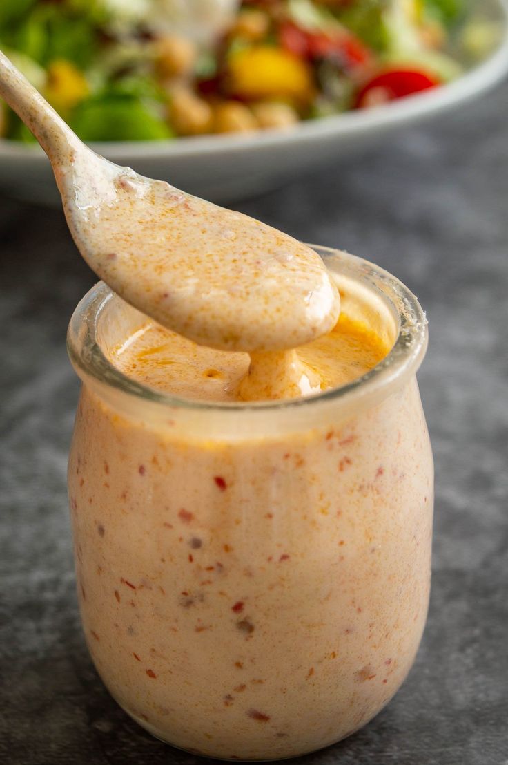 a spoon is sticking out of a jar filled with fruit and salad dressing next to a bowl of salad